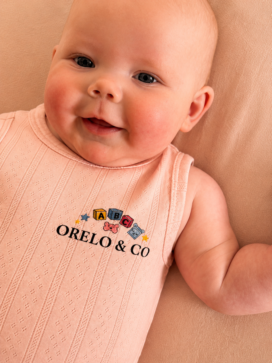 Baby wearing a pink sleeveless shirt with 'ORELO & CO' branding on a beige background